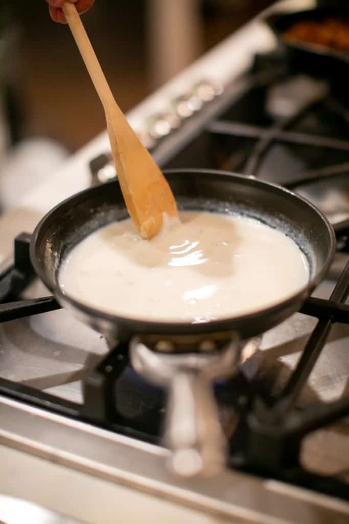 A pan of cream being stirred with a wooden spoon