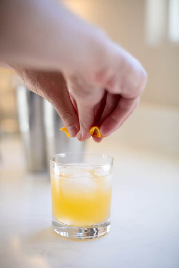A man squeezing an orange in to the cocktail