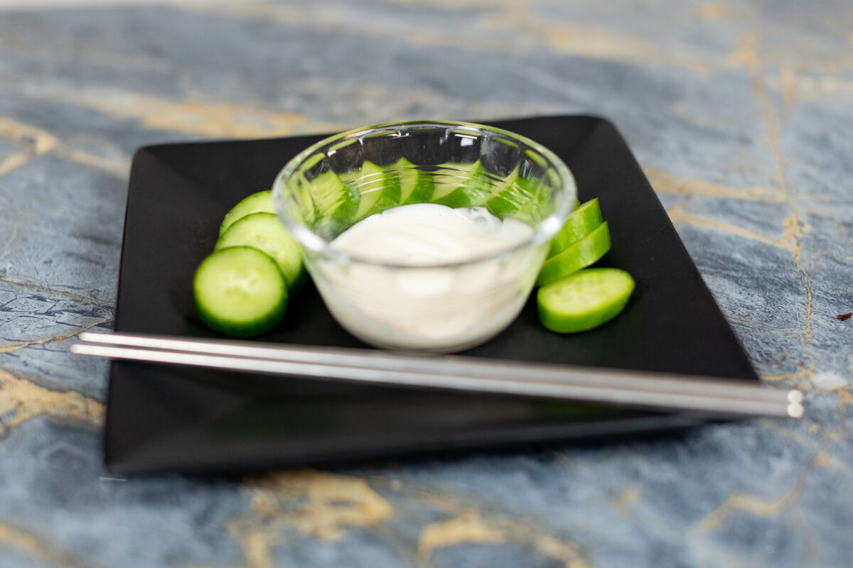 Cucumbers and Japanese white sauce on a black plate with metal chopsticks on top of a blue marble table