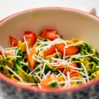 Basil spinach pesto pasta in a ceramic bowl garnish with parmesan cheese and tomatoes