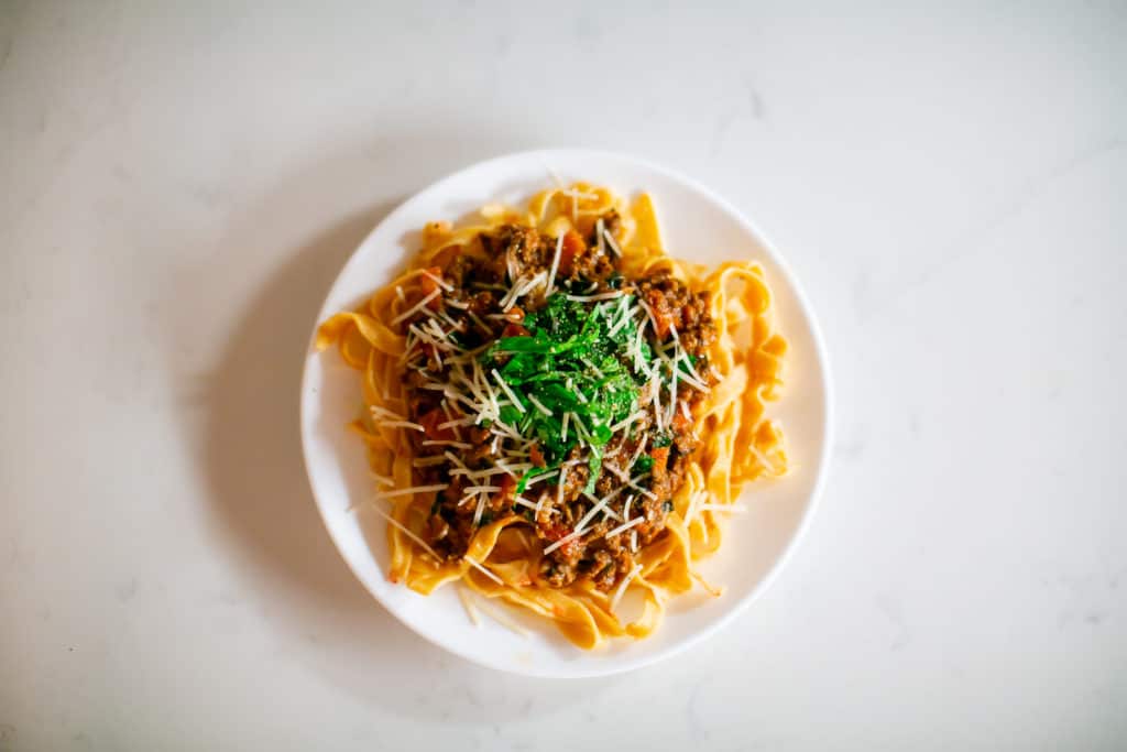 Beef bolognese pasta sauce garnished with herbs and parmesan cheese on a white plate