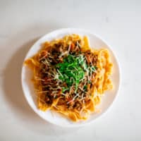 Beef bolognese pasta sauce garnished with herbs and parmesan cheese on a white plate