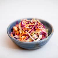 A blue cheese coleslaw in a blue ceramic bowl is placed on a white surface