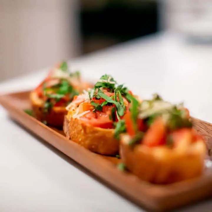 Three toasted bruschetta with tomatoes and herbs served on a brown wooden plate