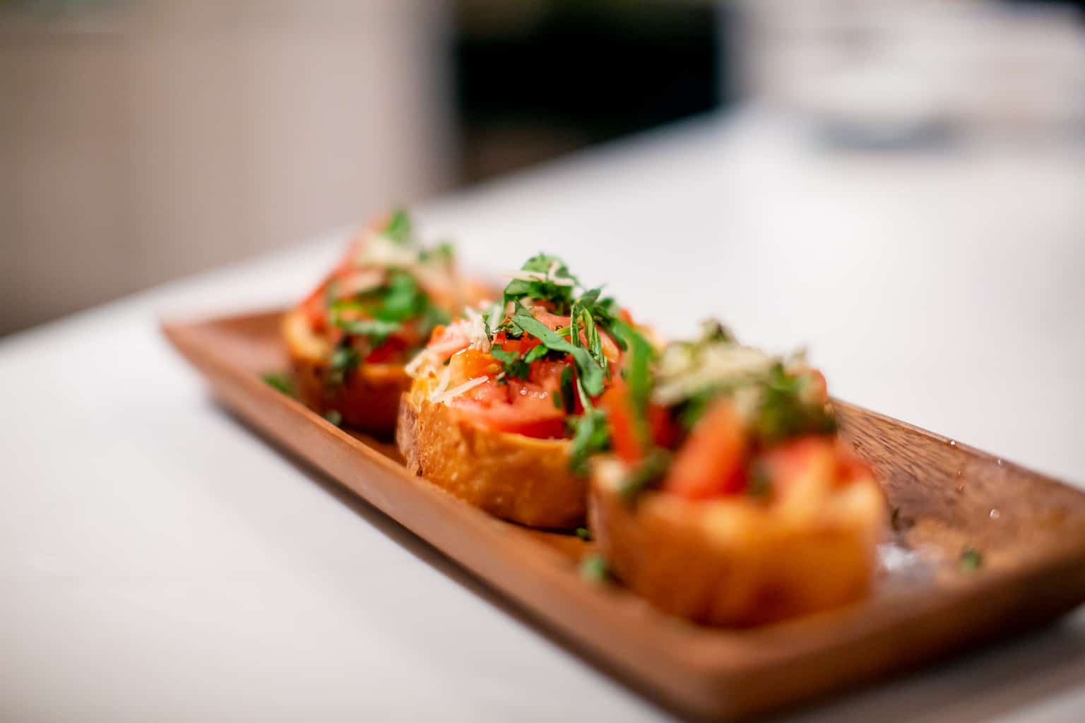 Three toasted bruschetta with tomatoes and herbs served on a brown wooden plate