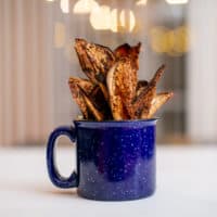 Baked crispy eggplant chips served on a blue ceramic mug placed on a white surface