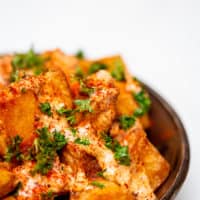 Close-up of fried patatas bravas served in a black bowl placed on a white wooden table