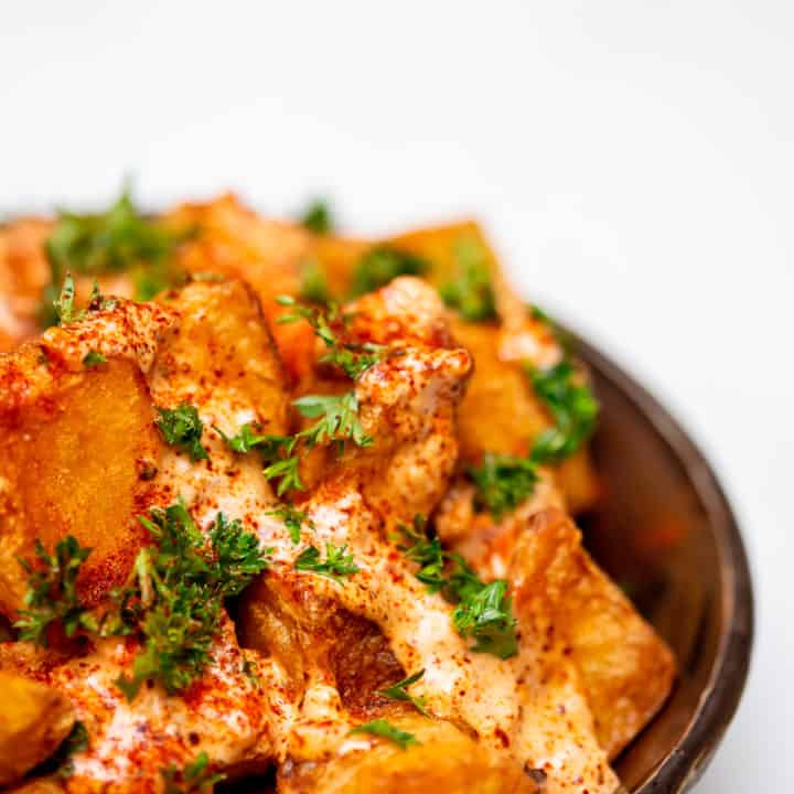Close-up of fried patatas bravas served in a black bowl placed on a white wooden table