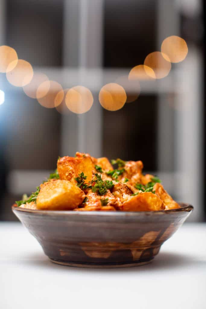 Fried patatas bravas tapas served on a bowl and topped with parsley