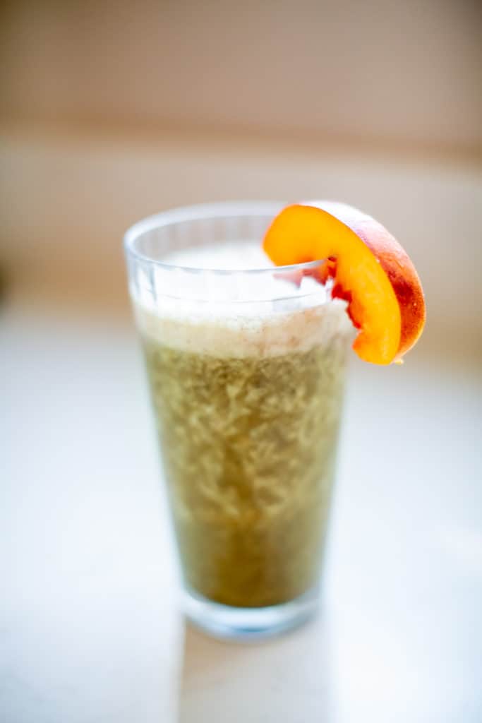 Blended green smoothie served with a peach slice