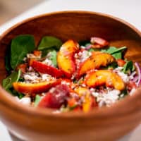 Grilled peach salad served in a brown wooden bowl placed on a white table