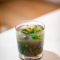 A cold lavender mojito served in a clear glass placed on a white table