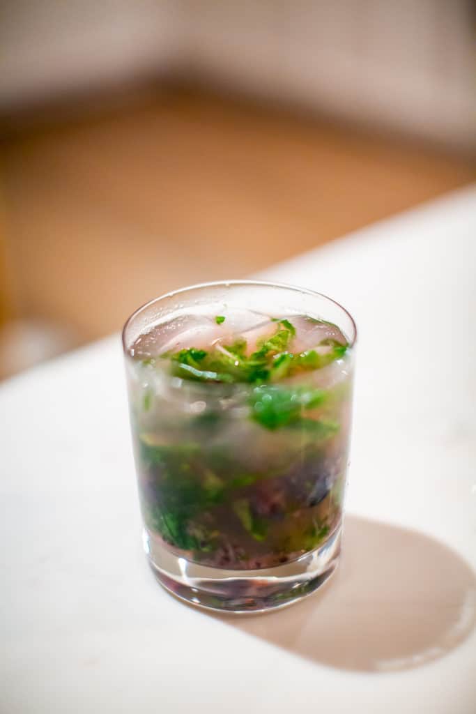A cold lavender mojito served in a clear glass placed on a white table