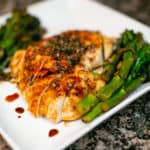 Oven baked chicken breast served with asparagus served on a white plate placed on a rough surface