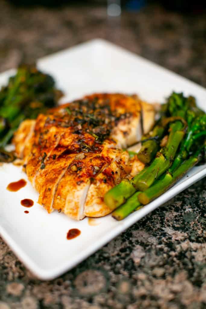 Oven baked chicken breast served with asparagus served on a white plate placed on a rough surface