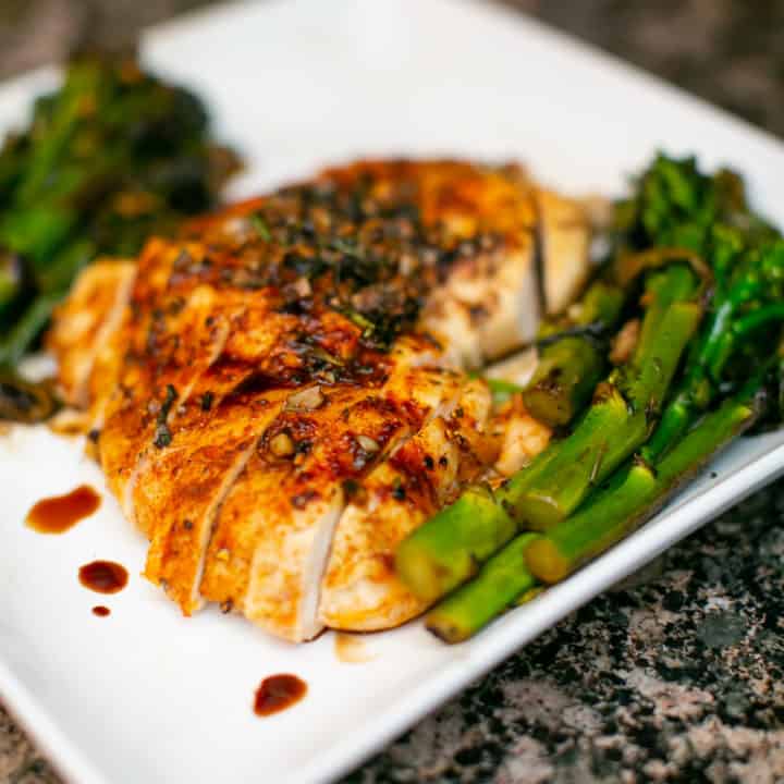 Oven baked chicken breast served with asparagus served on a white plate placed on a rough surface