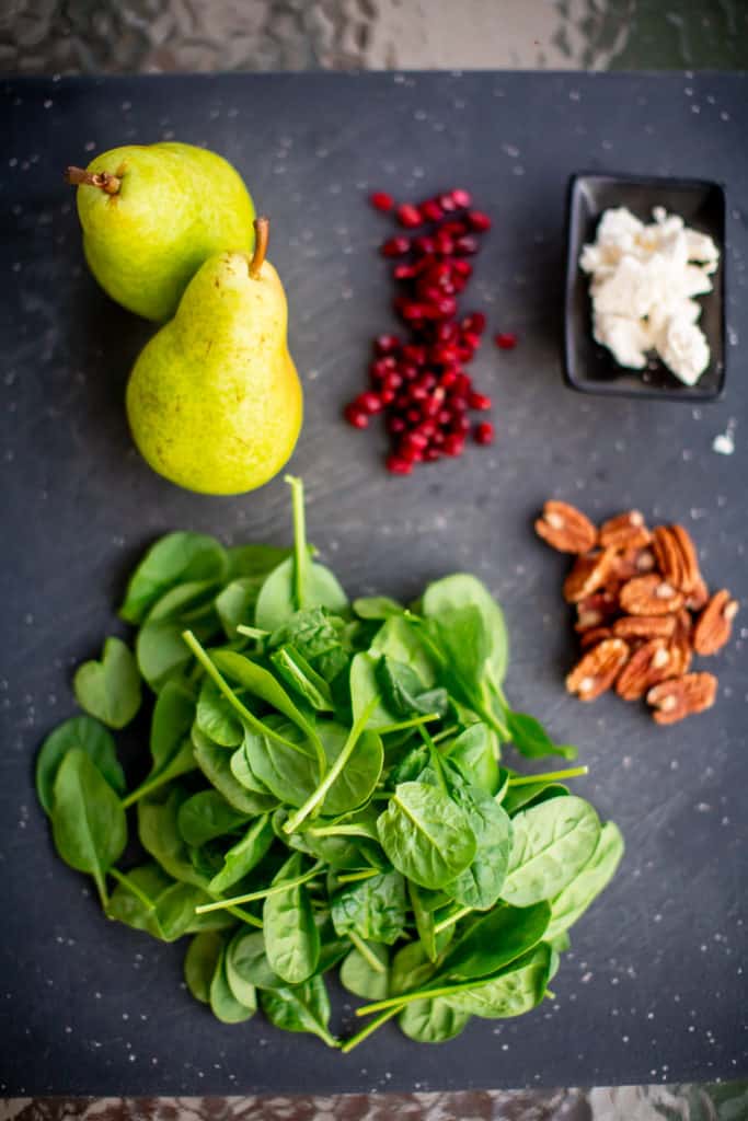 Ingredients for pear and pomegranate salad prepped over a black cutting board