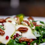 Pear and pomegranate salad topped with pecan nuts served on a white plate