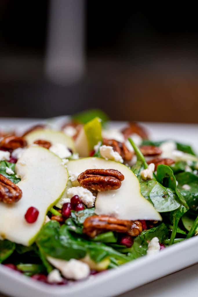 Pear and pomegranate salad topped with pecan nuts served on a white plate