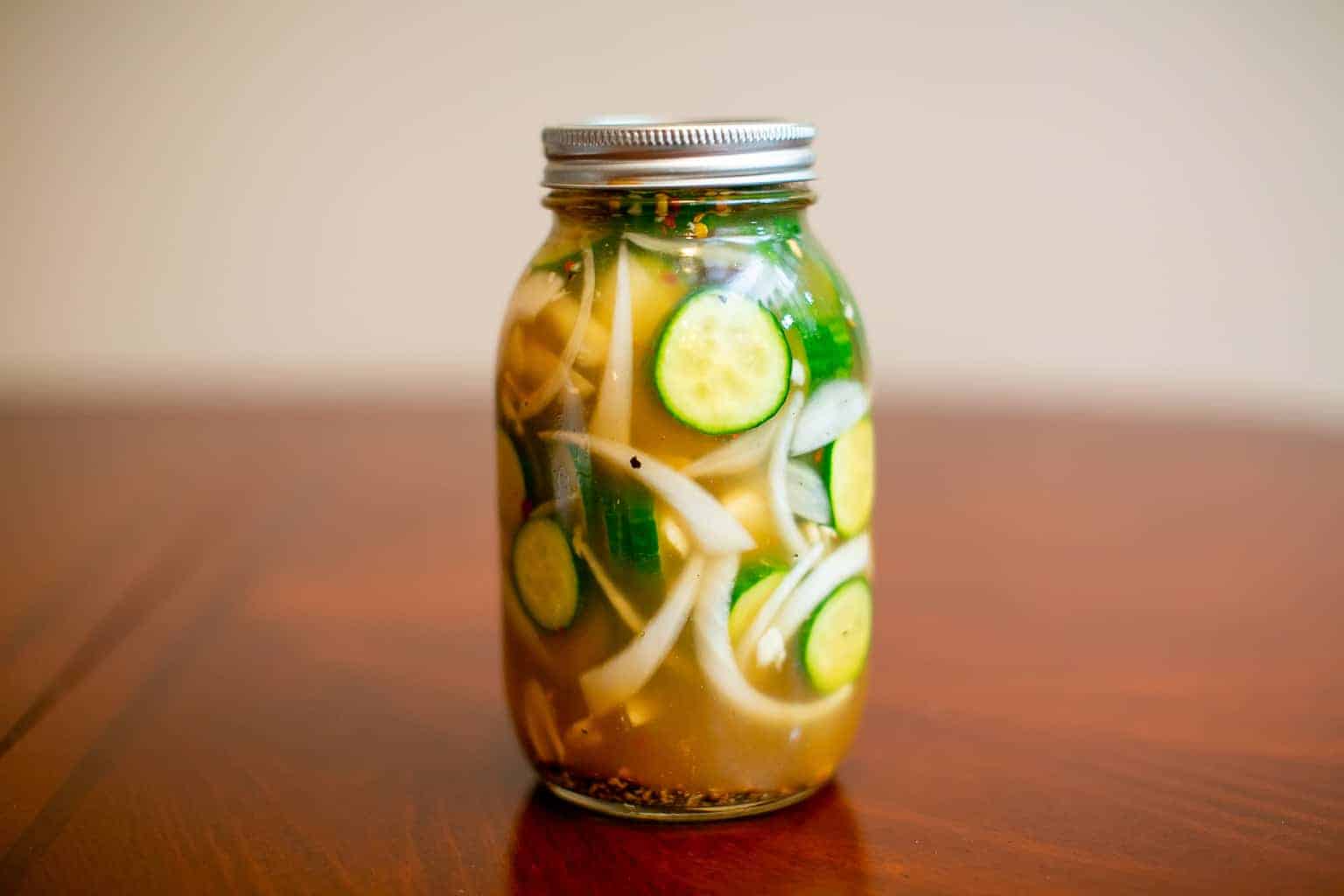 A closed jar full of spicy pickle juice placed on a brown wooden table