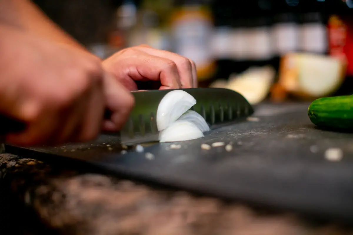 Man cutting an onion into small slices with a chef's knife on a black cutting board