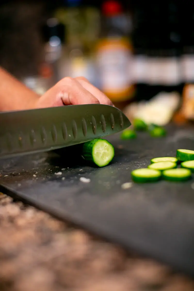 Man cutting cucumbers into medallions on a black cutting board with a chef's knife