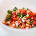 A spicy pico de gallo served in a white bowl placed on a white surface