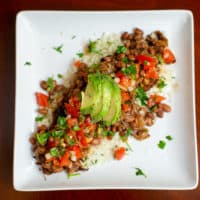 Pinto beans and chili lime rice topped with avocado and tomatoes served on a white plate placed on a brown wooden table