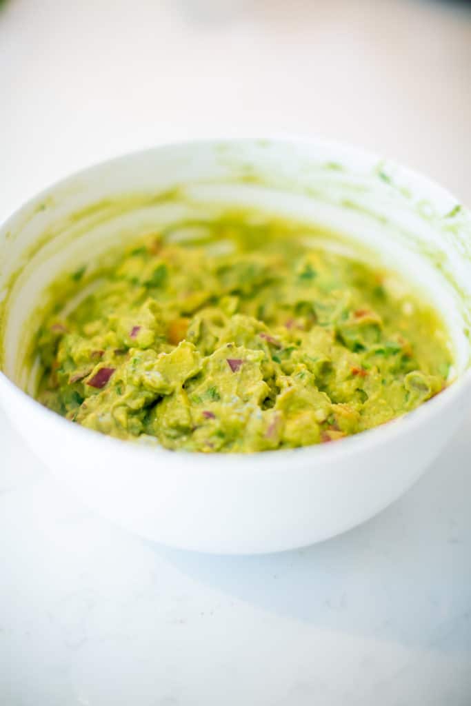 Close-up spicy guacamole served in a white bowl placed on a white table