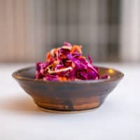 A brown ceramic bowl of sugar-free coleslaw placed on a white surface