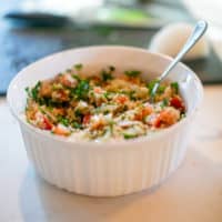 Tabouli salad served in a white bowl with a silver spoon placed on a white surface