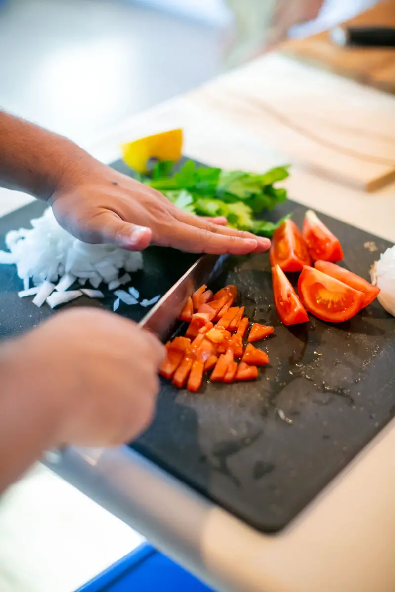 Man cutting tomatoes on a black cutting board with a knife that will be used in a tabouli salad
