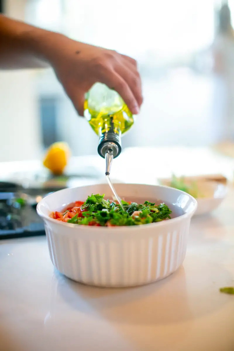 Drizzling olive oil into a bowl of Middle Eastern Tabouli Salad on a kitchen countertop