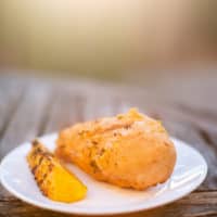 Pineapple teriyaki chicken with a sliced grilled pineapple served on a white plate placed on a wooden table