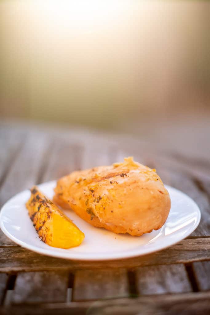 Pineapple teriyaki chicken with a sliced grilled pineapple served on a white plate placed on a wooden table