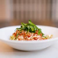 Pasta topped with spicy tomato sauce and herbs served in a white bowl placed on a white surface