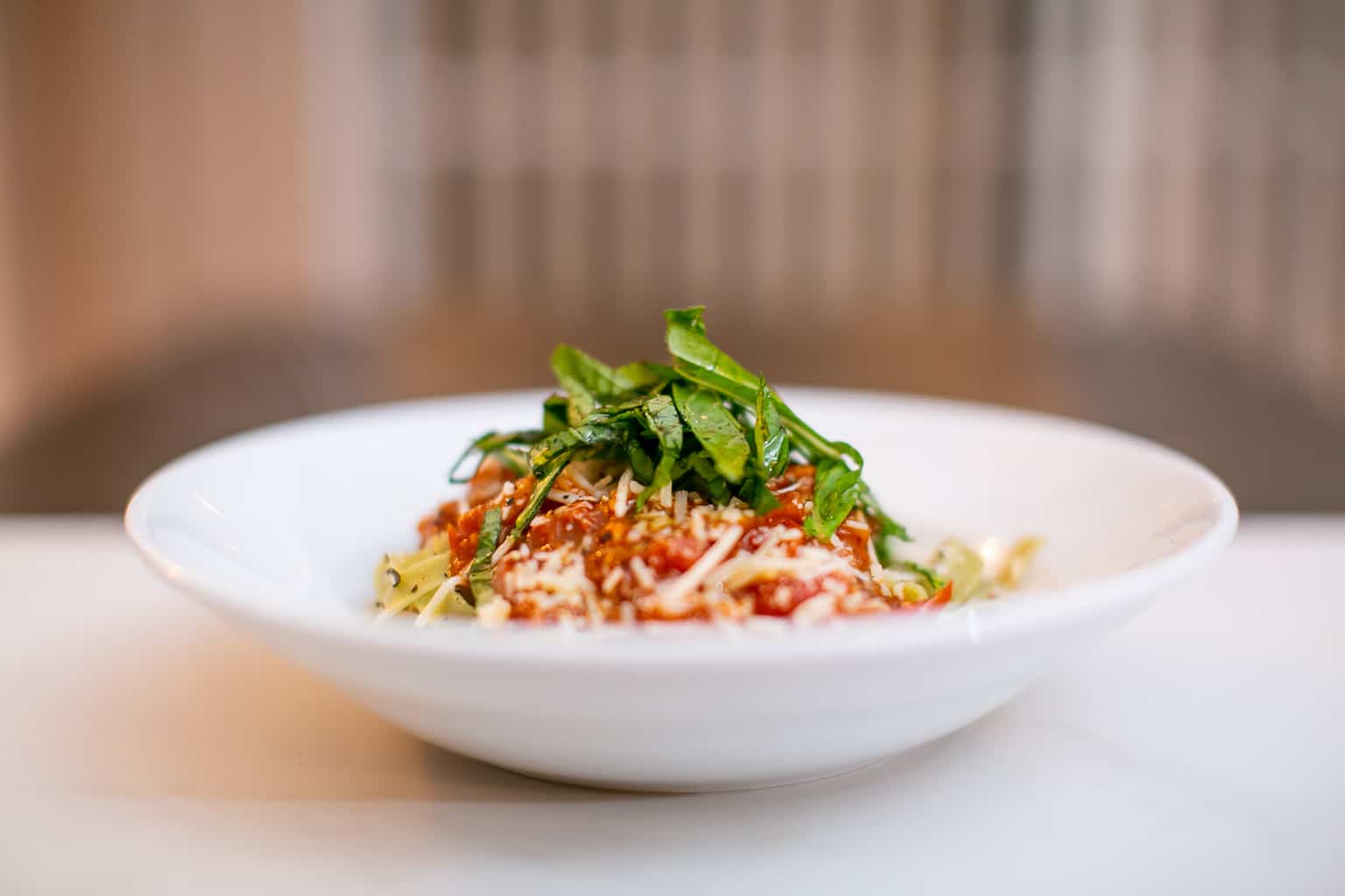 Pasta topped with spicy tomato sauce and herbs served in a white bowl placed on a white surface