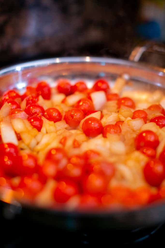 Cooking onions and cherry tomatoes on a pan until they break down