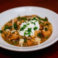 Close-up of spicy white bean chicken chili garnished with herbs served in a white bowl placed on a red table