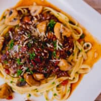 Fettuccine pasta with beef bourguignon garnished with herbs served on a white square plate placed on a wooden table