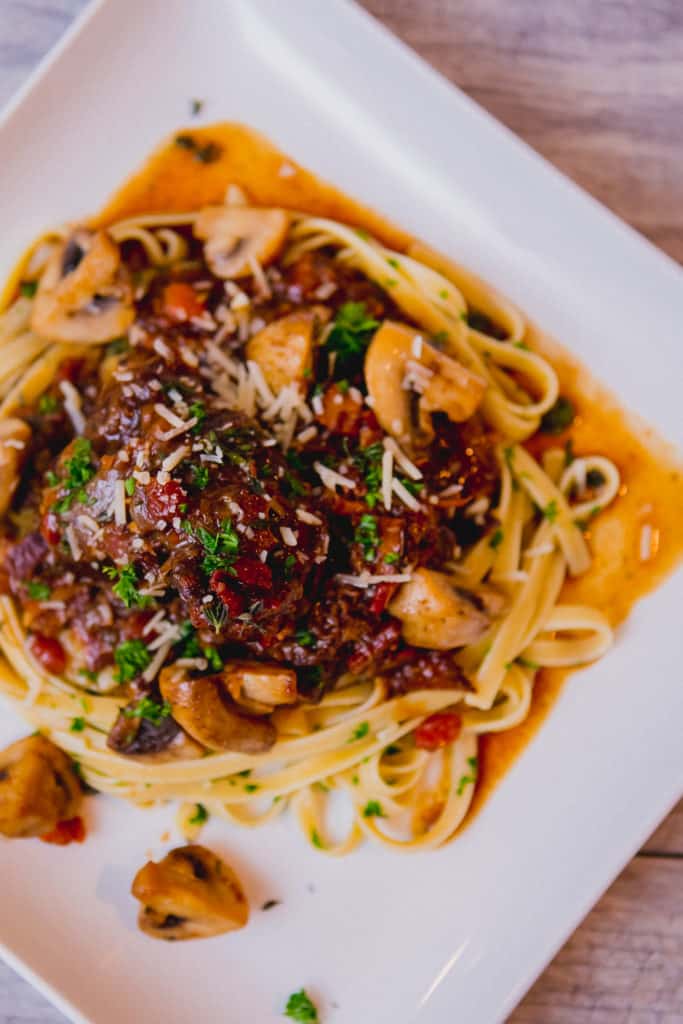Fettuccine pasta with beef bourguignon garnished with herbs served on a white square plate placed on a wooden table
