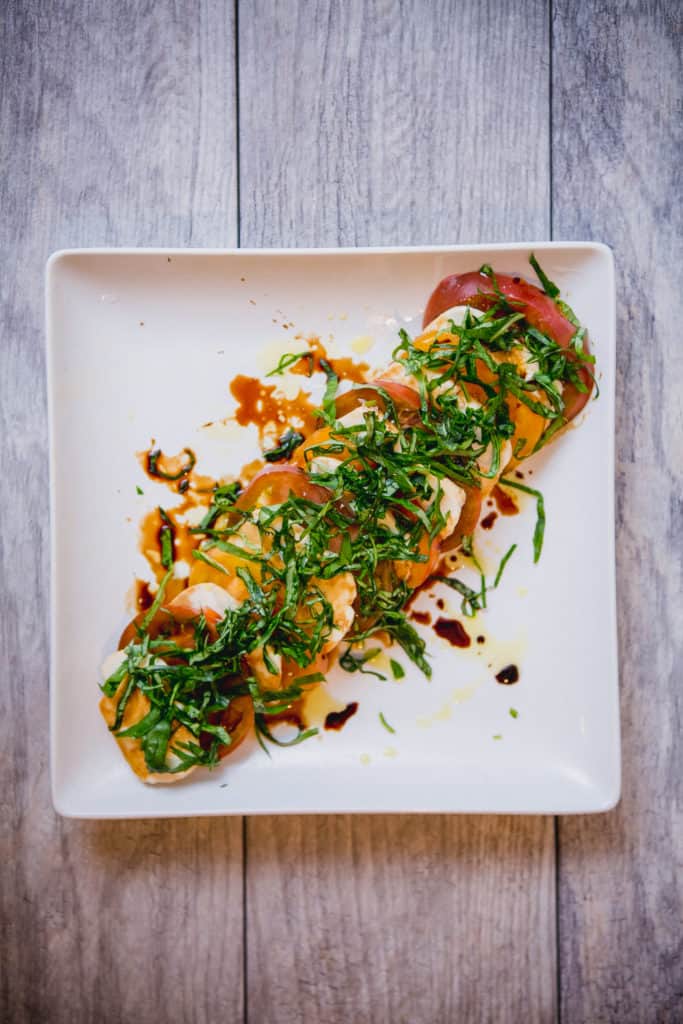 Caprese salad topped with basil and olive oil on a white plate