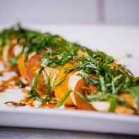 Close-up Caprese salad garnished with herbs and olive oil served on a white plate placed on a wooden table