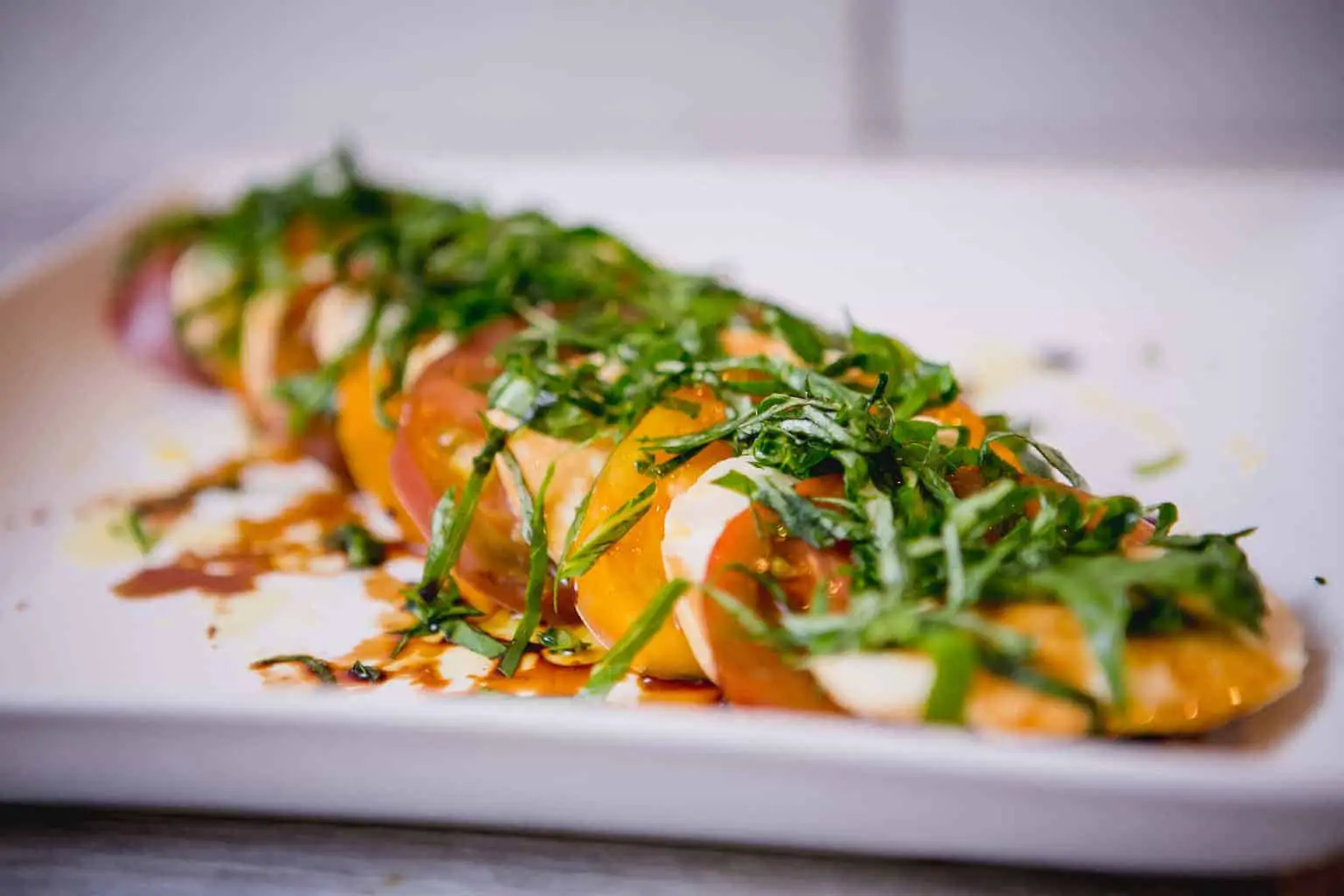 Close-up Caprese salad garnished with herbs and olive oil served on a white plate placed on a wooden table