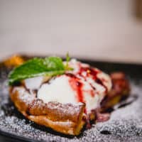 A slice of Dutch baby topped with vanilla ice cream and herbs served on a black plate