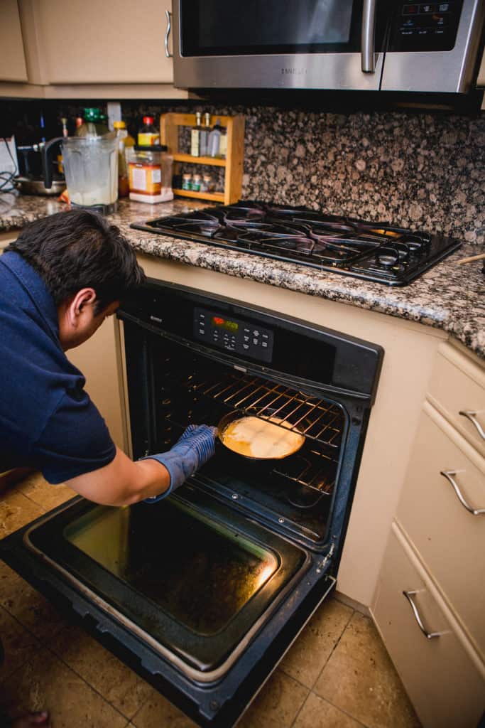 A man placing a batter of dutch baby into an oven