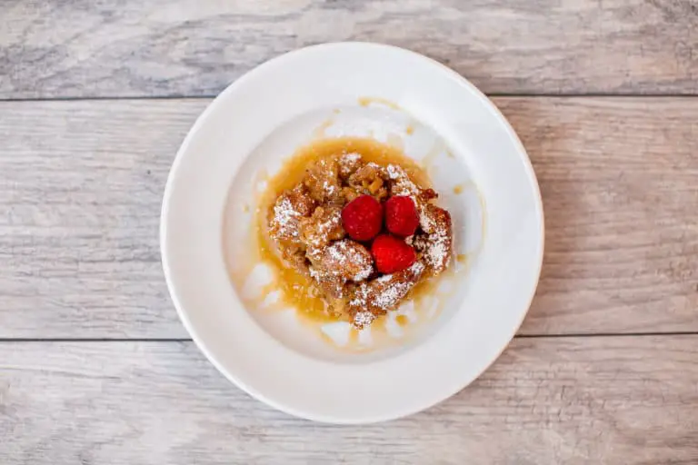 A white plate with churro bread pudding topped with raspberries placed on a wooden surface