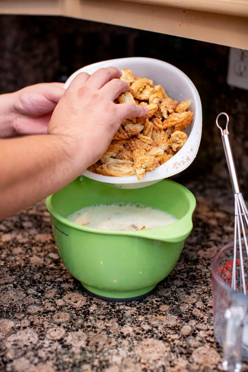 Man placing churros into the bread pudding mixture  in a green mixing bowl