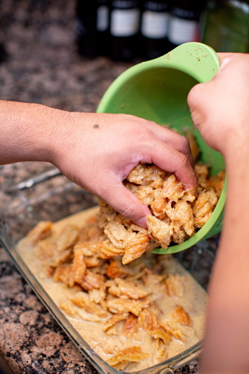 Man moving churros for bread pudding into a baking tray on a brown kitchen counter