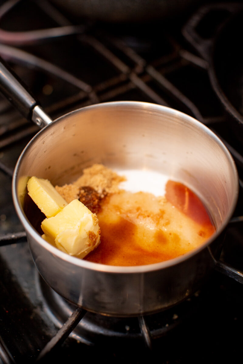 Bourbon, sugar, and butter melting together in a sliver pan on a stove